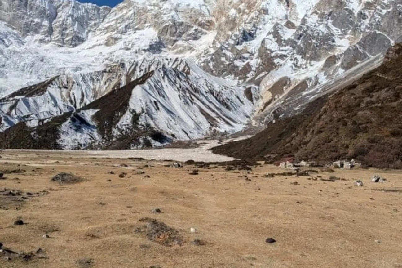 Expansive dry grassland valley beneath towering, massive snow-covered Himalayan peaks on the Popular Annapurna Circuit Trek Packages trail.
