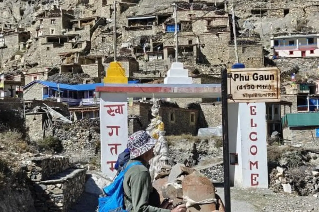 The welcoming gateway sign for Phu Gaun at 4150 meters with ancient stone houses built into the hillside behind it.