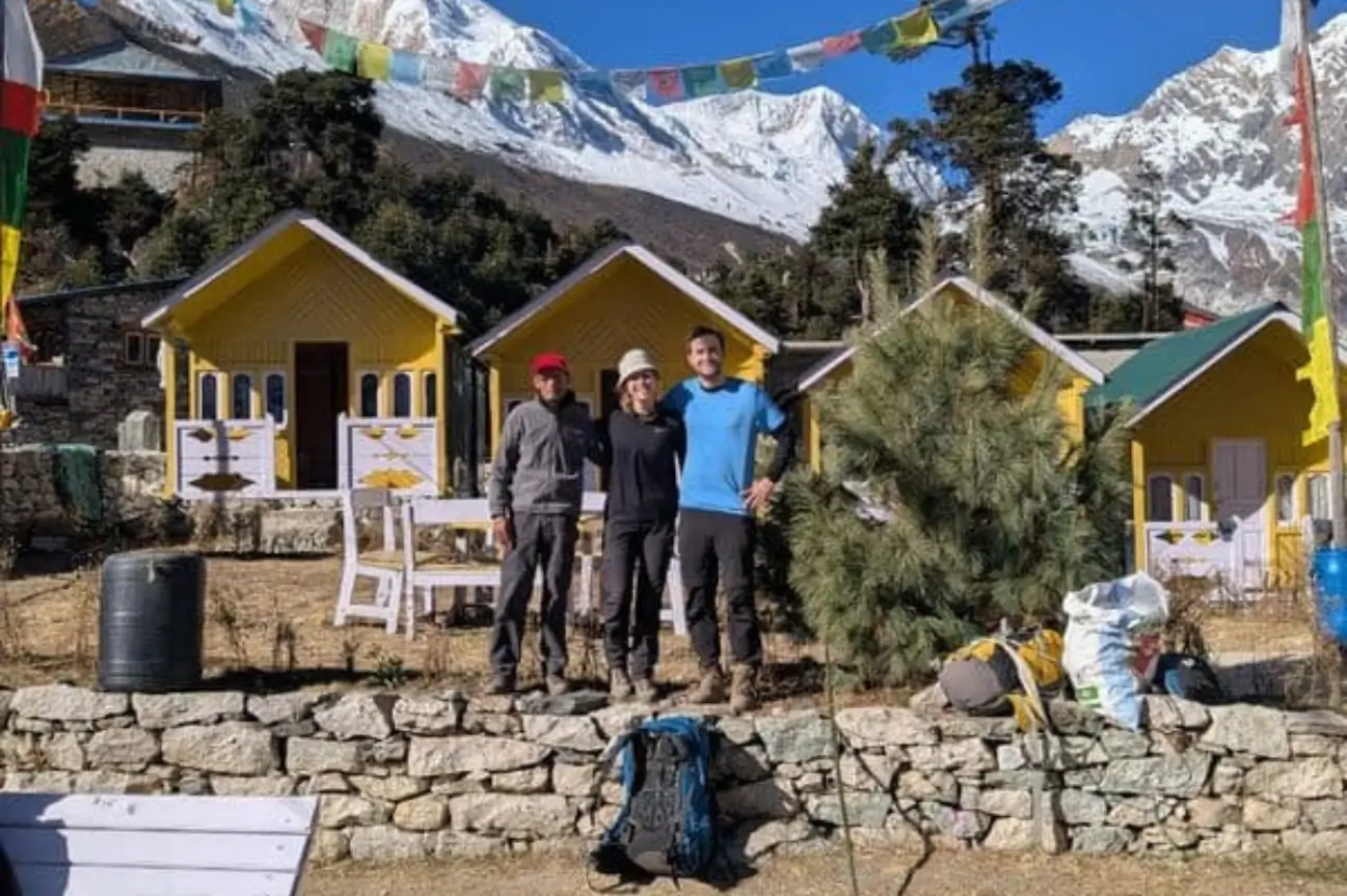 Trekkers posing outside colorful yellow wooden mountain lodges decorated with prayer flags during Tea House Treks.